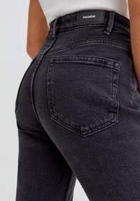 Jeans de mezclilla negros de talle alto con un diseño ajustado, que cuentan con un bolsillo trasero y detalles de costura sutiles. Etiqueta visible en la cintura.
