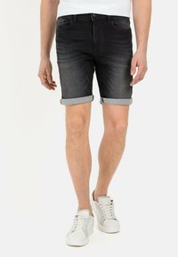 Schwarze Denim-Shorts mit umgekrempelten Säumen, Fünf-Taschen-Design und leichter Ausbleichung. Kombiniert mit weißen Turnschuhen vor neutralem Hintergrund.