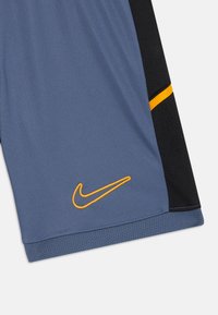 Nike-shorts i blått med svarte sider, med en oransje logo. Laget av lett stoff med en pustende mesh-textur.