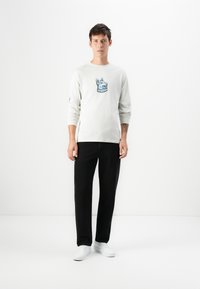 Lange mouwen lichtgrijs shirt met een blauwe grafiek van een hond, gecombineerd met zwarte rechte broek en witte sneakers. Minimalistisch ontwerp.