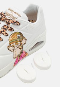 Weißer Sneaker mit einem gemusterten Leopardendruck-Schnürsenkel, der ein Cartoon-Affen-Design an der Seite und zwei zusätzliche weiße Schnürsenkel aufweist.