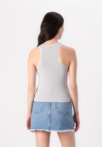 Gray ribbed tank top with wide armholes, paired with a blue denim mini skirt featuring a frayed hem and rear pockets.