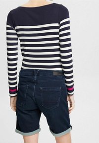 Top de manga larga a rayas en azul marino y blanco, combinado con shorts de mezclilla oscuros, con puños doblados y un sutil acento rosa en las mangas.