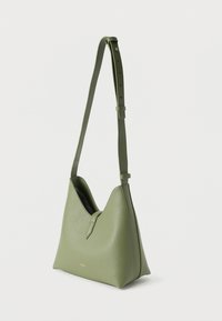 Πράσινη δερμάτινη τσάντα ώμου με ρυθμιζόμενο λουράκι, μινιμαλιστικό σχέδιο και μικρό χρυσό λογότυπο κοντά στη βάση, πάνω σε λευκό απλό φόντο.