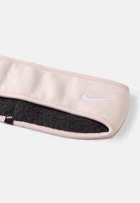 Faixa de cabeça Nike em tecido rosa suave, com um forro de fleece preto texturizado. Logotipo branco na frente e uma pequena etiqueta da marca na lateral.