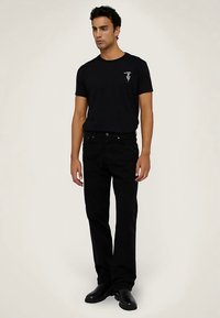 Czarna koszulka z małym nadrukiem na piersi, zestawiona z czarnymi spodniami. Strój ma dopasowany krój i gładką fakturę. Czarne buty dopełniają wygląd.