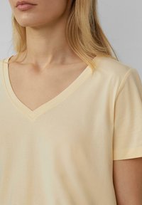 Lichtgele, kortaf T-shirt met V-hals, gemaakt van zachte stof met een gladde textuur en minimale stikseldetails langs de halslijn.