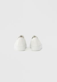 Baskets blanches avec une tige en cuir lisse, bout rond et semelle plate en caoutchouc. Conception à lacets avec col rembourré et détails subtils du logo.