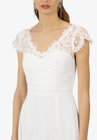 Witte jurk met een kant bodice, een V-hals en kapmouwen, een vloeiende rok en fijne kantafwerking bij de schouders.