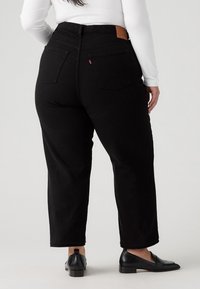 Vaqueros negros de cintura alta con corte recto, que cuentan con bolsillos traseros y una etiqueta de cuero en la cintura. Textura de denim suave.