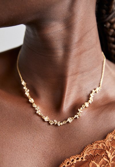 Collier en or avec un design floral, ornée de petites pierres précieuses transparentes, chaîne délicate et finition polie, porté autour du cou.