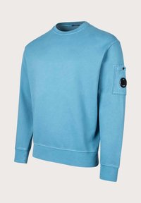 Felpa di cotone blu con collo a giro, maniche lunghe e tasca a toppa sul braccio sinistro con dettaglio a bottone circolare.