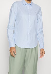 Himmelblaues Langarmhemd mit spitzem Kragen, Knopfverschluss und Logo-Stickerei auf der Brust. Aus glattem Baumwollstoff gefertigt.