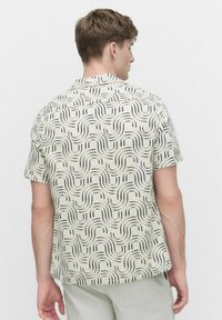 Korte mouwen shirt in lichtbeige stof met een zwart golvend patroon, standaard kraag en een rechte zoom. Geen zichtbare sluitingen.