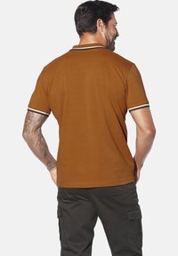 Braunes Polo-Shirt mit slim Fit, ausgestattet mit weißen und schwarzen gestreiften Akzenten am Kragen und an den Ärmeln. Hergestellt aus weichem Baumwollstoff.
