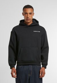 Zwarte sweatshirt met kap. Bevat het "KARMA CLUB" logo in het wit op de borst, een voorkeurszak en ribgebreide boorden en onderrand. Zachte stoffen textuur.