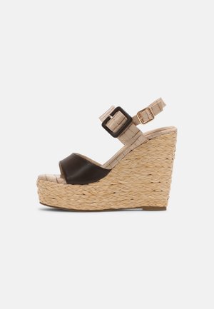Sandale compensée beige avec plateforme en paille tissée, bride noire ouverte sur les orteils et bride de cheville beige ajustable avec deux boucles.