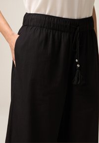 Zwarte, lichte broek met een elastische tailleband, zijzakken en een koord met metalen accenten en een kwastje.
