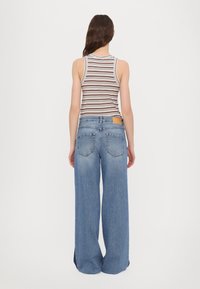 Wide-leg blue jeans made of denim, featuring back pockets and a tan leather patch at the waistband. Paired with a striped sleeveless top.