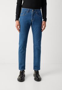 Blå denim jeans med en klassisk pasform, der har fem lommer, kobbertråd og en frontknaplukning. Kombineret med sorte lædersko.