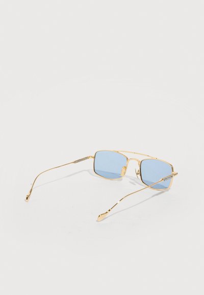 Rectangular blue-tinted lenses with thin gold metal frames and temples, resting open on a plain light background.