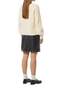 Beige Strickpullover mit Rippstruktur und puffartigen Ärmeln, kombiniert mit einem schwarzen Kunstlederrock, Knöchelsocken und schwarzen Schuhen.