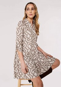 Beige und cremefarbener knopfartiger Kleid mit geometrischem Muster, das eine lockere Passform, lange Ärmel und ein gestuftes Rockdetail bietet.