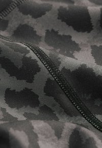 Crni sportski materijal s suptilnim uzorkom leopardove kože. Glatka tekstura s kontrastnim crnim šavovima duž šava.