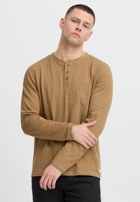Dugi rukav, smeđa henley majica s teksturiranim završetkom, koja ima placket s tri dugmeta i mali logo detalj na prsima.