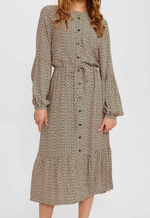 Woman in a beige long-sleeve midi dress with black and brown small spots, front buttons, elastic waist, and gathered hem.