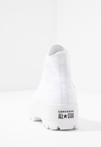 Bílé vysoké plátěné tenisky s texturovaným povrchem, platformovou podrážkou a černým logem "CONVERSE ALL★STAR" na patě.