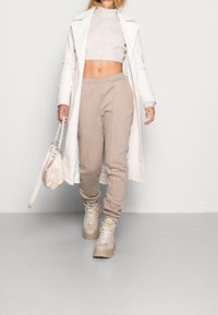 Beige sweatpants met plooien, gecombineerd met een cropped lichtgrijze trui en een witte jas. Beige high-top sneakers en een kleine tas maken de look compleet.