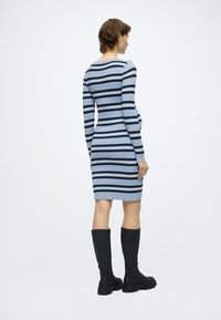 Πλεκτό φόρεμα με μακριά μανίκια, με ρίγες σε μπλε, ανοιχτό μπλε και ναυτικό μπλε. Ζευγάρι μαύρες μπότες μέχρι το γόνατο. Λεπτή υφή, εφαρμοστή γραμμή.