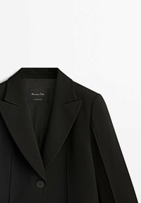 Blazer noir à un seul bouton avec revers crantés posé à plat sur une surface blanche, montrant une partie du col et des manches.