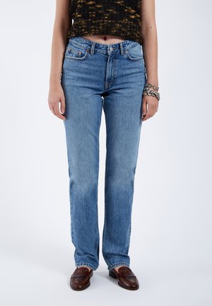 Light blue straight-leg jeans with a classic five-pocket design and subtle fading, made from denim fabric. Worn with brown loafers.