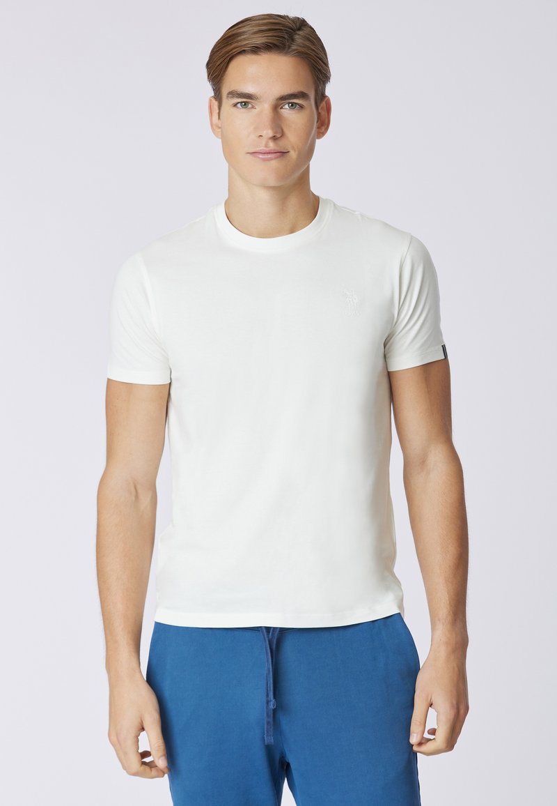 T-shirt bianco a maniche corte con scollo rotondo, realizzato in tessuto morbido, caratterizzato da un logo discreto sul lato sinistro del petto e un design semplice.