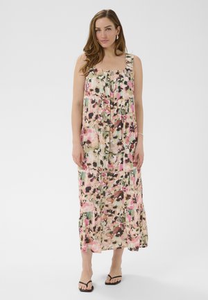 Woman standing wearing a sleeveless, floral-patterned, ankle-length dress with square neckline and black sandals on a white background.