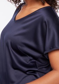 Marinblus i satin med lös passform, V-ringning, korta ärmar och mjuk textur. Har subtila sidsömsdetaljer för en extra touch av stil.
