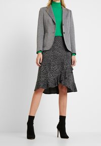 Blazer grigio dal design strutturato, abbinato a un dolcevita verde e a una gonna nera con stampa leopardata e orlo arricciato. Stivaletti neri alla caviglia.