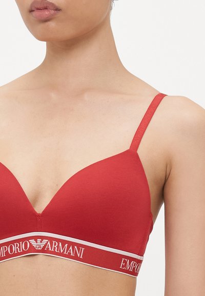 Sarkanais trīsstūrveida krūšturis, izgatavots no gludas auduma, ar zīmolu elastīgu joslu baltā krāsā, uz kuras ir rakstīts "EMPORIO ARMANI", kā arī plānām regulējamām siksniņām.