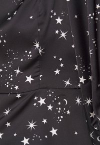 Tela negra con patrones de estrellas y lunas blancas. Varias formas y tamaños de estrellas crean un diseño disperso con una textura suave.