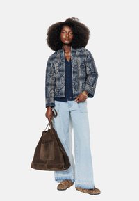 Veste bleue à motifs avec des manches longues, un cardigan sombre en dessous, un jean large bleu clair, et un sac tote en daim marron. Chaussures à imprimé animal.