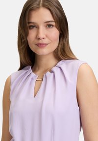 Fialová bezrukávová blúzka s výstrihom v tvare kľúčovej dierky, náGatherovaním na ramenách a malým zlatým akcentom pri výstrihu.