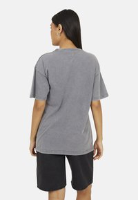 T-shirt gris surdimensionné à manches courtes, en mélange de coton, avec des coutures visibles et une coupe décontractée, associé à un short en denim noir.