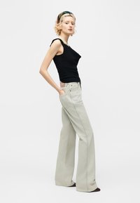 Γυναίκα με κοντά σγουρά ξανθά μαλλιά, φορούσε μαύρο αμάνικο τοπ, μπεζ τζιν φαρδιάς γραμμής, περιδέραιο με πέρλες και εμπριμέ κορδέλα για τα μαλλιά.