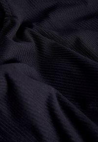 Juodas tekstūruotas audinys su vertikaliomis briaunomis, demonstruojantis minkštus klosčius ir nukareną. Medžiaga atrodo lengva ir glotni su subtiliu blizgesiu.