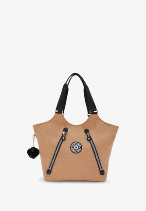 Tan-Tasche mit schwarzen Reißverschlüssen und Akzenten, mit einem runden Logo und einem schwarzen Pom-Pom-Schlüsselanhänger. Hergestellt aus glattem Material.