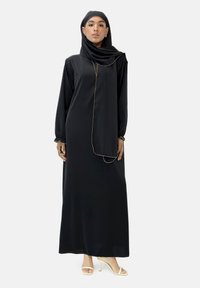 Schwarzes Kleid mit langen Ärmeln und fließender Silhouette, ergänzt durch einen passenden Hijab und goldene Akzente entlang des Ausschnitts.