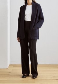 Mjölnarblå stickad cardigan med öppen framsida, två fickor och ribbad textur, ihopparad med svarta högmidjade byxor och svarta loafers.