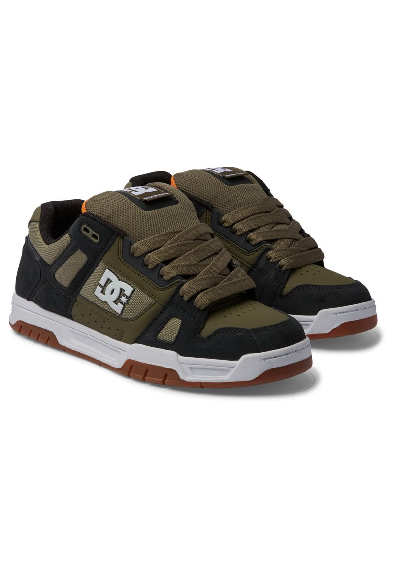 Schwarze und olivgrüne Sneaker aus Mesh und Wildleder, mit einer weißen Zwischensohle, brauner Gummisohle und prominentem DC-Logo.
